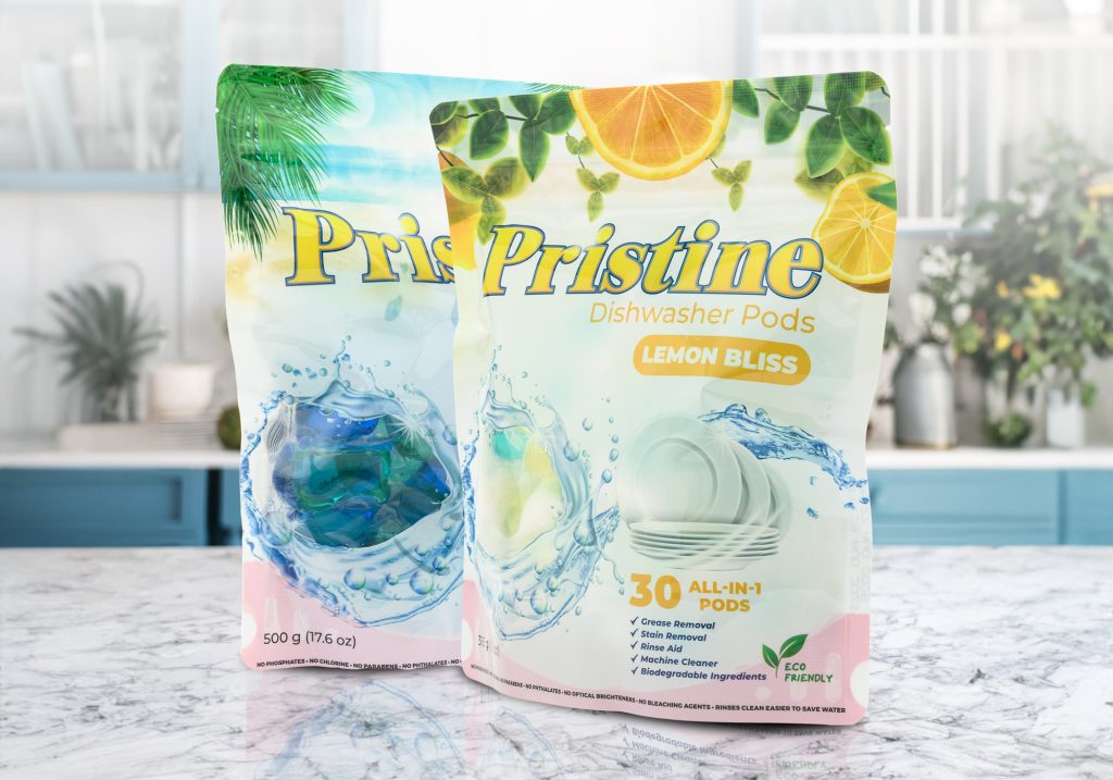 Two Pristine Dishwasher Pods pouches featuring Island Breeze and Lemon Bliss variants, with tropical-themed packaging and all-in-one cleaning claims displayed in a kitchen setting.