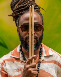 Modupe Onilu holding a drumstick vertically between his eyes.