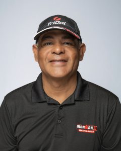 Derek Daniel in a TriDot cap and black IronMan Certified Coach polo, facing camera with a slight smile.